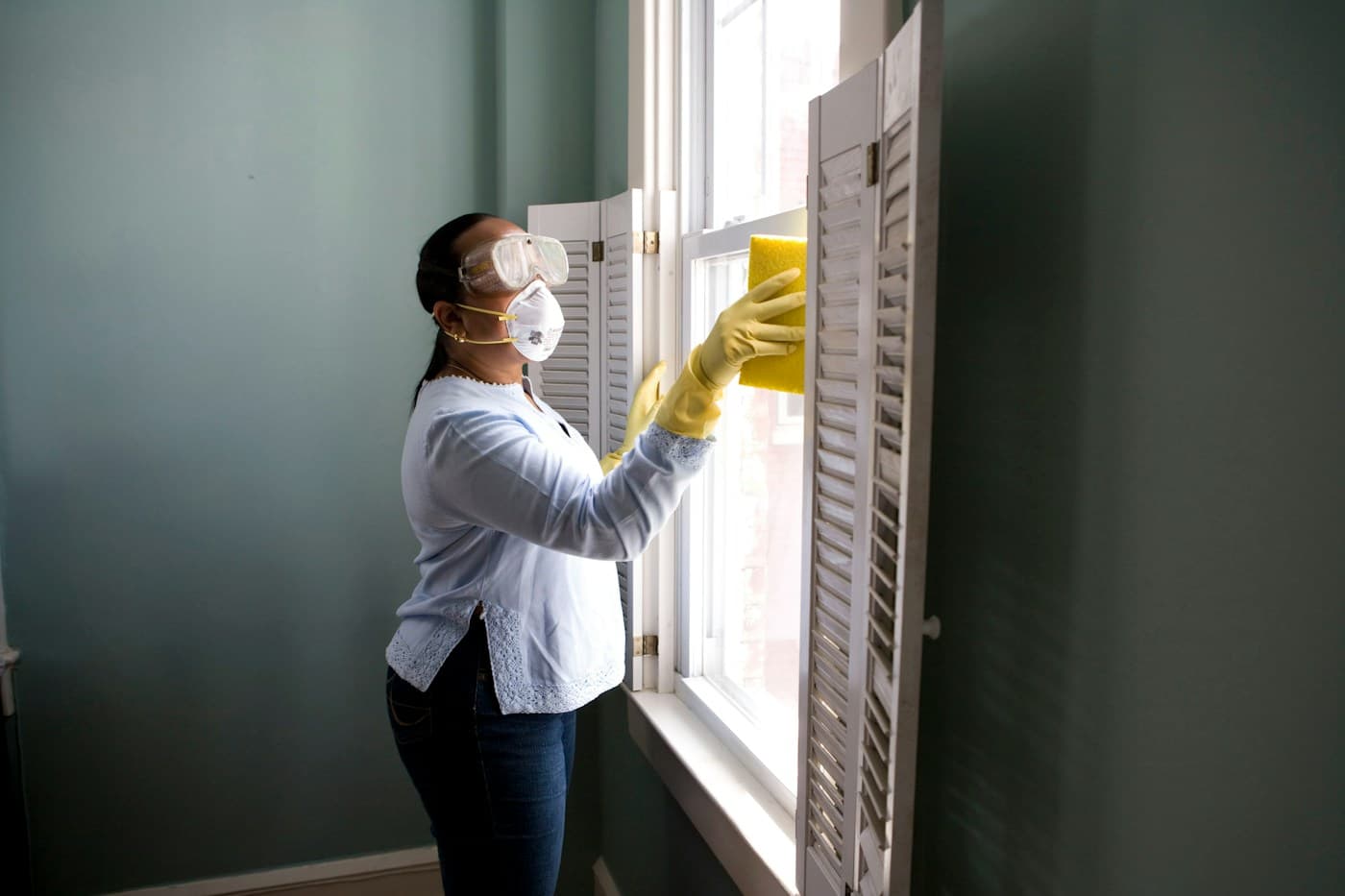 A cleaner wearing protective gloves and goggles wipes window shutters